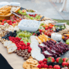 table covered by assortment of food such as meats, cheeses, nuts, fruits, and vegetables.