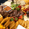 table covered by assortment of food such as meats, cheeses, nuts, fruits, and vegetables.