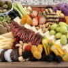 Assortment of meats, cheeses, fruits, and vegetables on a charcuterie board.